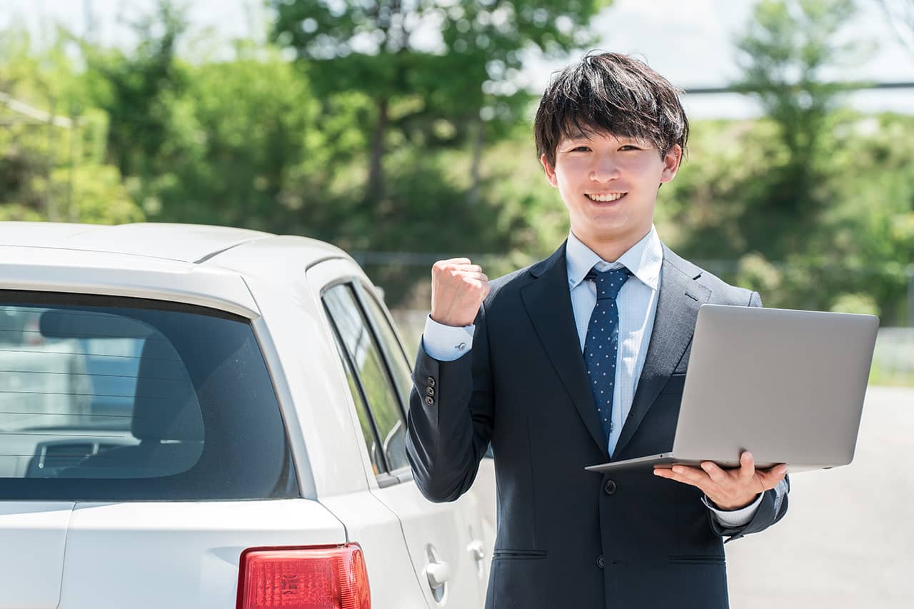 車の横でPCを片手に笑顔の男性